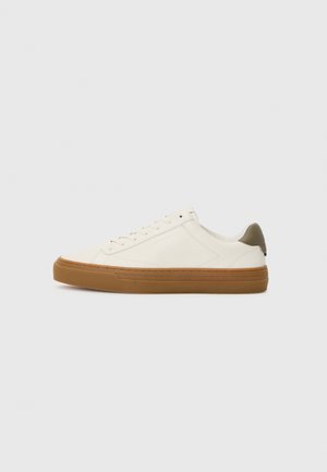 White leather sneaker with a rounded toe, rubber gum sole, and olive green heel accent. Features lace-up closure and minimal stitching.