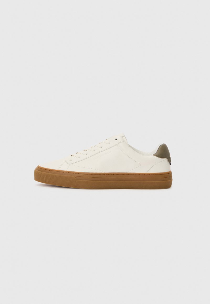 White leather sneaker with a rounded toe, rubber gum sole, and olive green heel accent. Features lace-up closure and minimal stitching.