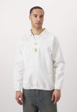 Weißer Pulloverjacke mit einem kragenförmigen Ausschnitt, gerippten Bündchen und elastischem Saum. Mit goldfarbenem Logo-Detailing auf der Brust.