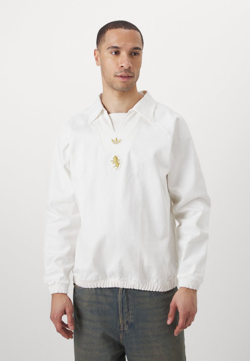 Bílá pulovrová bunda s límečkem, žebrovanými manžetami a elastickým lemem. Obsahuje zlaté logo na hrudi.