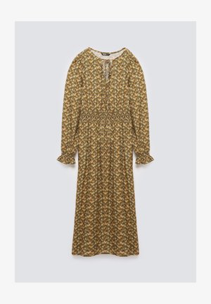 Lungo vestito floreale con sfondo marrone, caratterizzato da motivi gialli e verdi, vita arricciata, maniche lunghe e scollatura rotonda con dettaglio annodato.