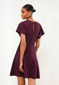 Ein kurzärmliges, burgunderrotes Kleid mit einem ausgestellten Rock. Es hat eine Schlüsselöffnungsdetails am Rücken und ein tailliertes Oberteil. Glatte Stoffstruktur.