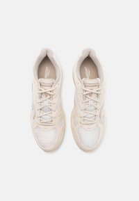 Weiße Mesh-Sneaker mit beige Akzenten, flachen Schnürsenkeln und einer gepolsterten Sohle. Mit einem Logo auf der Zunge und strukturierten Überzügen an den Seiten.
