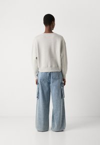 Lysegrå genser med avslappet passform og ribbestrikket kant, sammen med høyt liv og vide blå denim cargo-bukser som har sidelommer.
