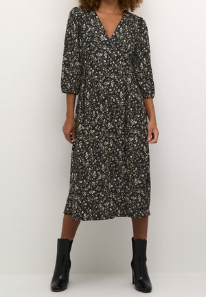 Robe midi noire à motifs floraux avec décolleté en V, manches trois-quarts et taille froncée. Associée à des bottines noires brillantes pour un contraste.