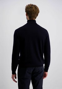 Marinefarbener Rollkragenpullover, gerippte Bündchen und Kragen, weiche Stricktextur, enganliegendes Design, getragen mit dunklen Hosen, von hinten betrachtet.