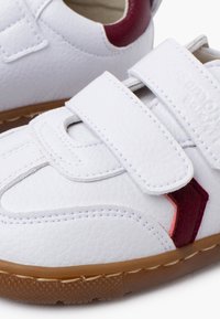 Scarpe sintetiche bianche con una finitura testurizzata, dotate di due cinturini in velcro, dettagli color bordeaux e una suola in gomma.