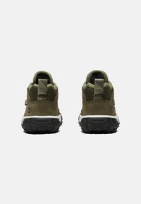 Chaussures de randonnée en suede vert et mesh avec une semelle en caoutchouc noir texturé, dotées d'une languette en tissu et d'une marque au niveau du talon.