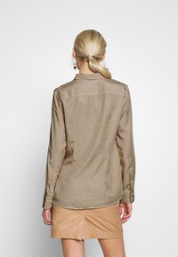 Tan silk shirt with a button-down collar, long sleeves, and a curved hem. Paired with a beige leather skirt, showing smooth texture.