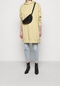 Sweat-shirt à capuche kaki, sac bandoulière noir, jean bleu clair et bottines noires. Le sweat-shirt présente une coupe décontractée et des manches longues.