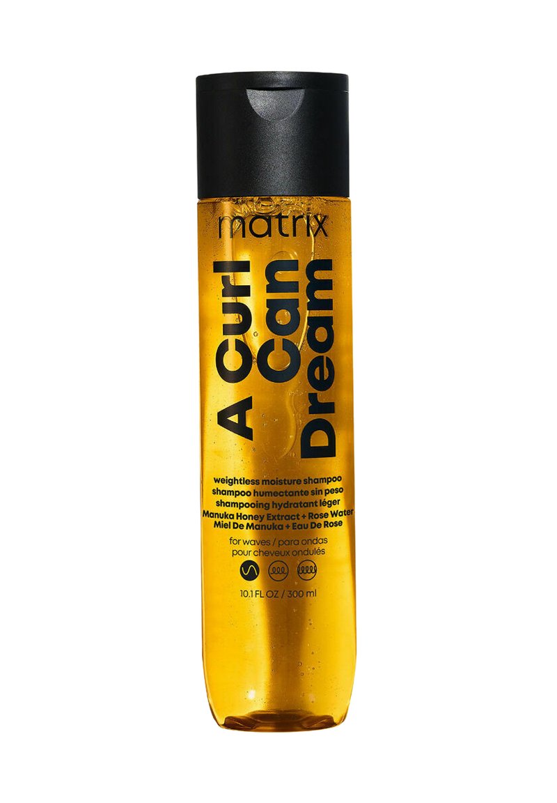 Heldere plastic fles met een zwarte dop, gevuld met een oranje vloeistof. Het etiket toont "A Curl Can Dream" en details over de kenmerken van de shampoo.