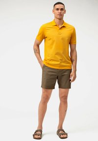 Geel polo-shirt met korte mouwen, beige shorts en bruine sandalen, met een ontspannen pasvorm en een gladde textuur.