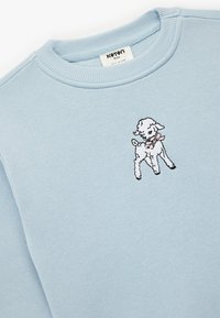 Ljusblå sweatshirt med en svartvit broderad lamm med en rosa rosett framtill. Mjuk textur och ribbad halsringning.