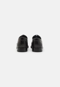 Zapatos de vestir de cuero negro con un acabado suave, punta redonda y tacón bajo, que presentan un detalle de logo en relieve en la parte trasera.