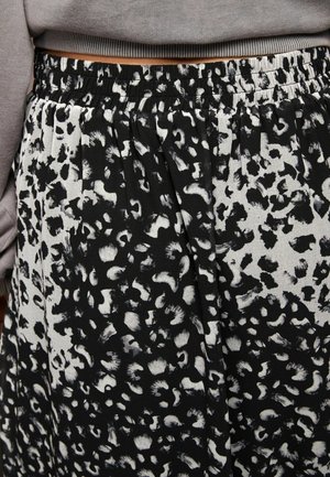 Jupe à imprimé léopard noir et blanc avec taille élastique portée avec un haut gris à manches longues, laissant apparaître un espace au niveau du ventre.