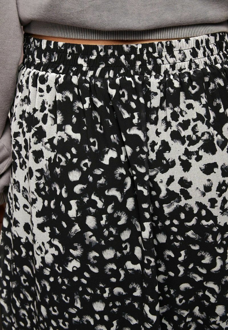 Jupe à imprimé léopard noir et blanc avec taille élastique portée avec un haut gris à manches longues, laissant apparaître un espace au niveau du ventre.