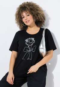 Camiseta negra con un dibujo en línea blanca de un personaje con ojos grandes y un lazo. Tela de algodón suave, corte relajado, mangas cortas.