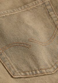 Tissu en denim beige avec une poche arrière cousue comportant des détails de fil orange courbé et une texture de tissage diagonal visible.