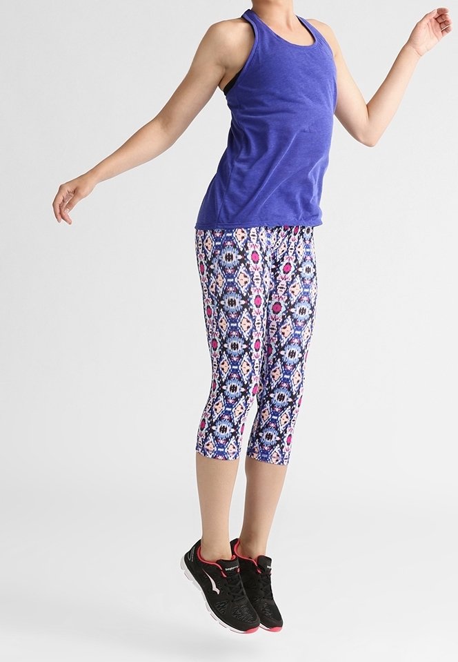 Personne en débardeur violet et leggings capri à motifs sautant en l'air, portant des chaussures de sport noires avec des accents rouges.
