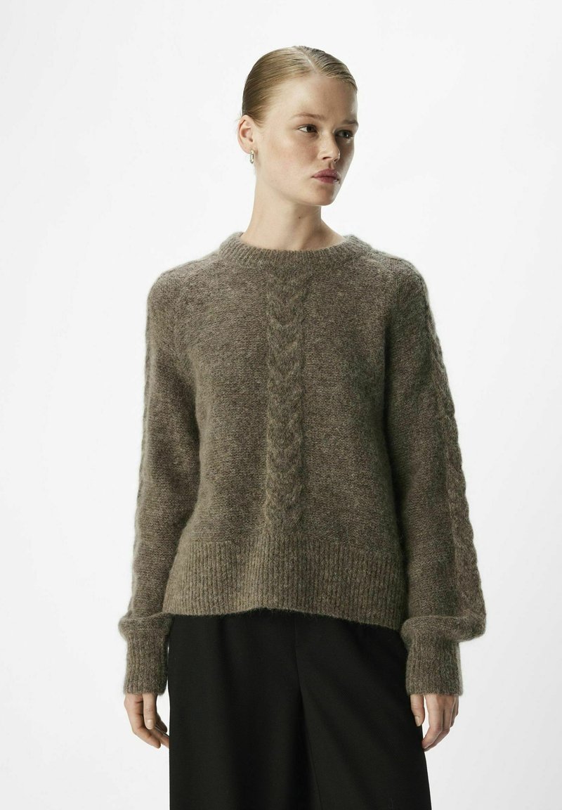 Maglione in mohair marrone con motivo a treccia al centro, polsini a coste e vestibilità rilassata, abbinato a pantaloni neri.