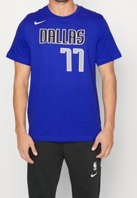 Modrá sportovní tričko s tučným černým nápisem "DALLAS" a šedou "77" na přední straně. Vyrobeno z měkkého materiálu, s kulatým výstřihem.