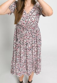 Robe fleurie avec un décolleté en V, manches courtes, taille cintrée et jupe fluide arborant un motif floral multicolore sur fond sombre.