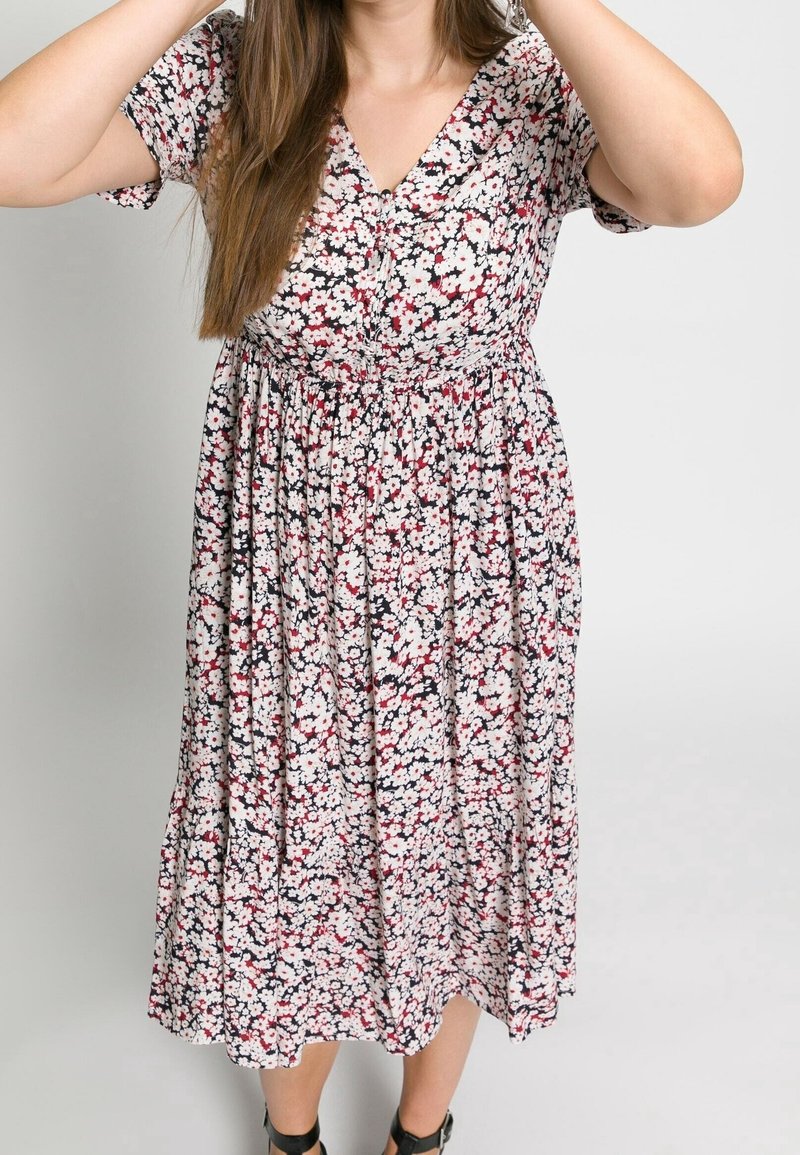 Robe fleurie avec un décolleté en V, manches courtes, taille cintrée et jupe fluide arborant un motif floral multicolore sur fond sombre.
