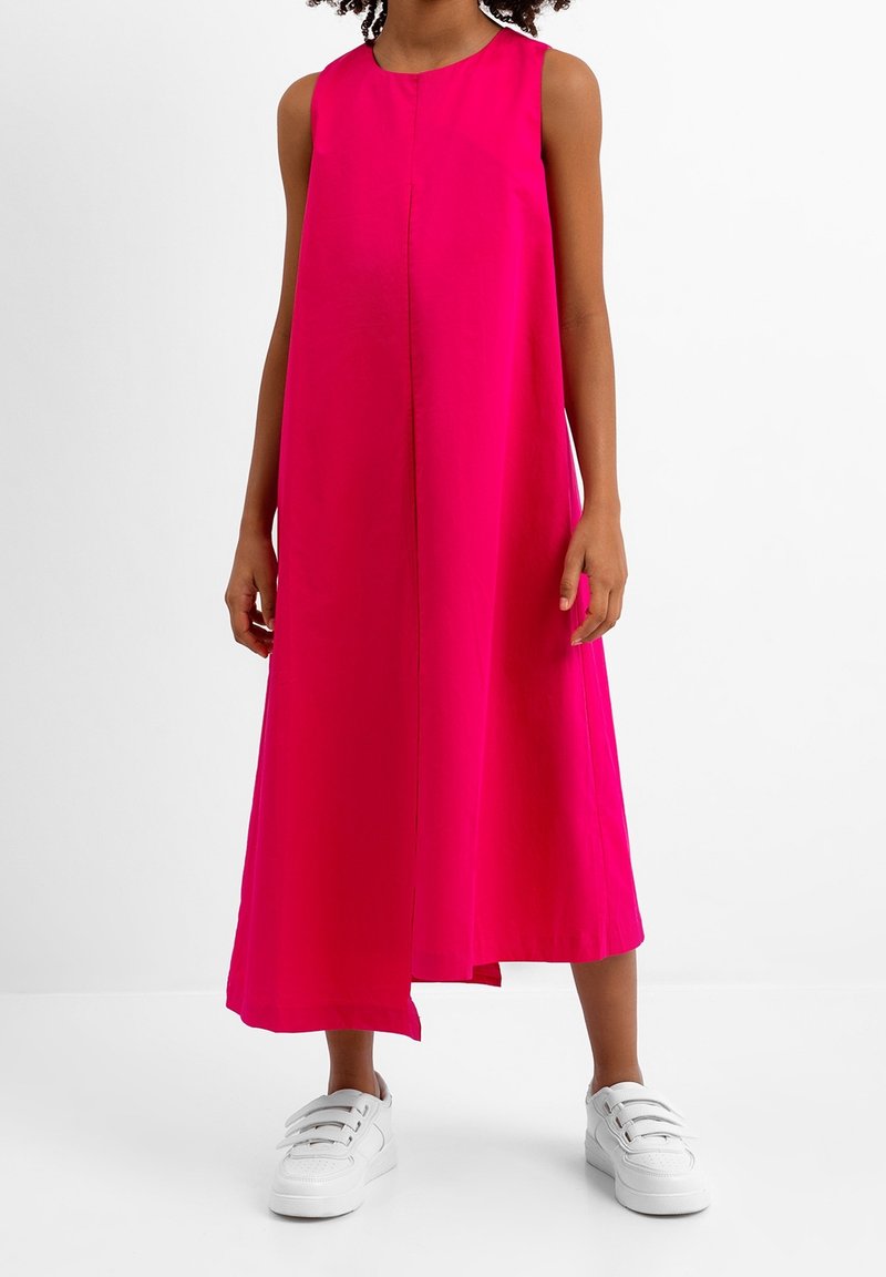 Fuchsiové šaty bez rukávů s rovnou siluetou, délka ke kolenům a středový šev, spárované s bílými teniskami.
