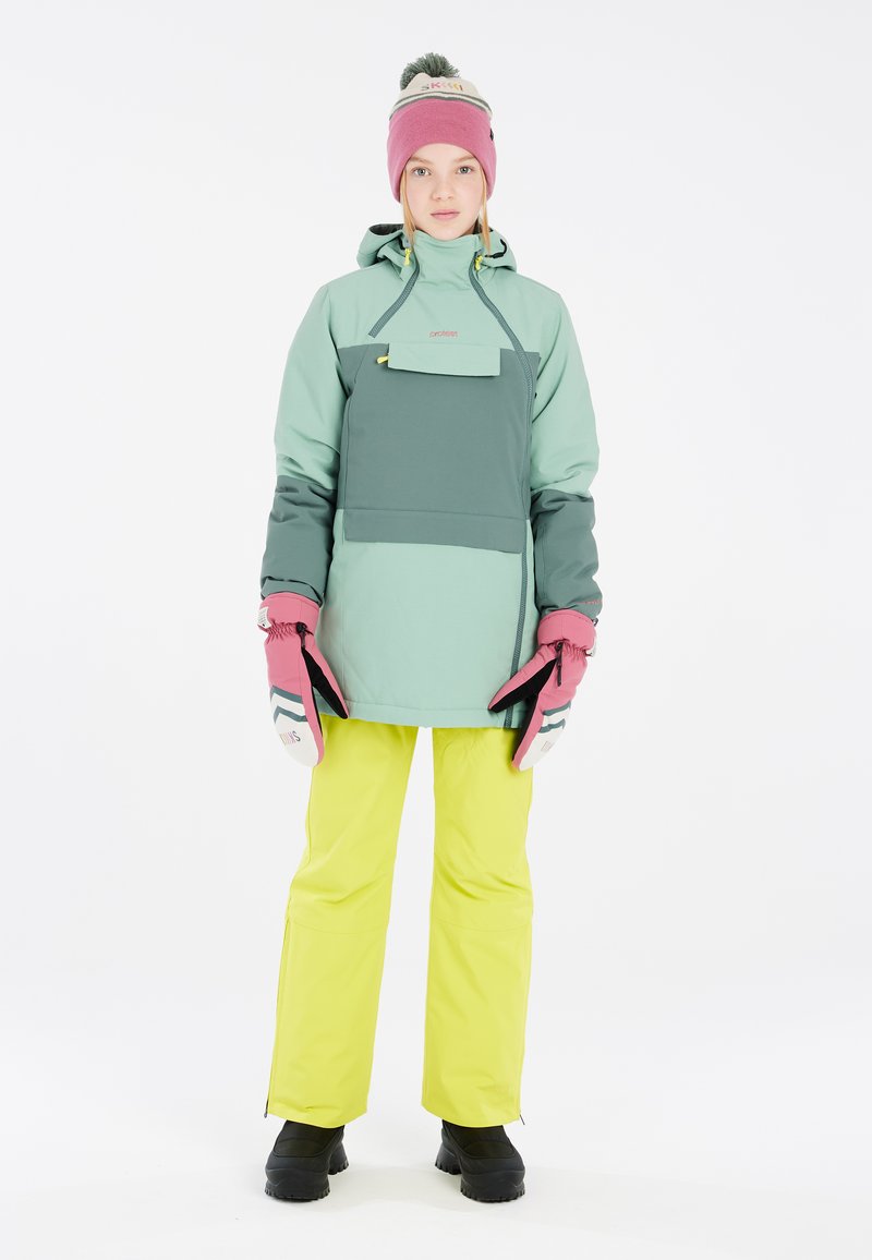 Conjunto de invierno que incluye una chaqueta verde bicolor con un bolsillo, pantalones amarillos brillantes, guantes rosas y un gorro rosa con un pompón.