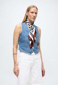 Jeans brezrok s prilegajočo obliko, v izrezu v obliki črke V, z gumbnim zapiranjem in sprednjim žepom. Nošen z rjavo-belim svilenim šal s potiskom.