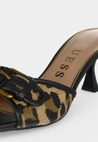 Μαύρο mule με τακούνι και λεοπάρ εμπρός μέρος, διακοσμητική μαύρη αγκράφα και μπεζ πάτος με την επωνυμία "GUESS" με χρυσά γράμματα.