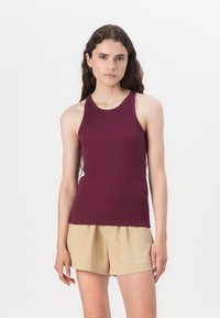 Burgundy sleeveless tank top with a fitted design, ribbed texture, and a round neckline, paired with beige shorts.
