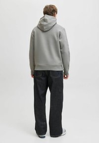 Sudadera de algodón gris con un bolsillo canguro en la parte delantera, combinada con jeans de pierna ancha de mezclilla oscura. Ambas prendas presentan un diseño casual y relajado.