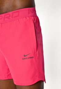 Rosa sportshorts med en strækbar talje, prydet med "NIKE PRO" embossing og et sort Nike swoosh-logo nederst på siden.