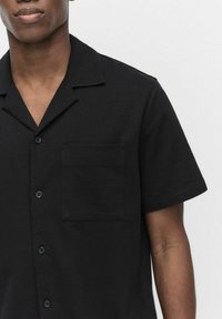 Zwarte shirt met korte mouwen in een gestructureerde stof, met een kraag, een enkele borstzak en zwarte knopen.