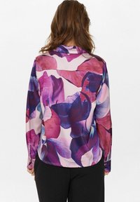 Langärmlige Bluse mit floralem Muster in Rosa-, Lila- und Blautönen auf hellem Hintergrund; glatte Textur, klassischer Kragen.