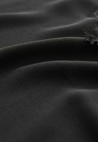 Tissu noir à texture lisse, présentant des plis doux et un éclat subtil, avec des détails de couture complexes sur un bord.