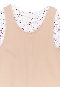 Hellbraunes Cordkleid mit breiten Trägern, über einem weißen Shirt mit kleinen floralen Mustern in Pink, Blau und Grün getragen.