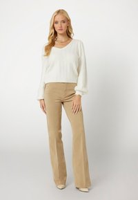 Suéter blanco de punto con escote en V, combinado con pantalones acampanados de pana beige con botones laterales. Tejido texturizado con un ajuste relajado.