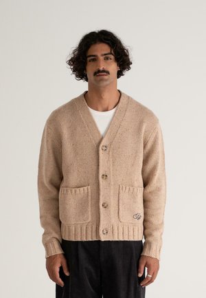 Beige Strickcardigan mit V-Ausschnitt, zwei aufgesetzten Taschen und braunen Knöpfen. Mit geripptem Saum und subtiler gesprenkelter Textur.