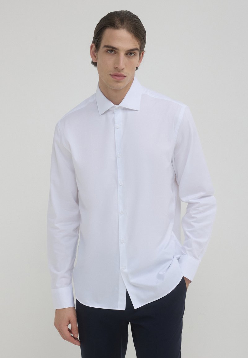Camicia bianca a maniche lunghe con bottone frontale, colletto a punta e trama liscia. Vestibilità su misura, adatta per abbigliamento formale o semi-formale.