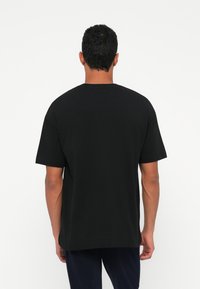 T-shirt de algodão preto com decote redondo, mangas curtas e um corte relaxado. Textura suave com barra reta; sem padrões ou detalhes visíveis.