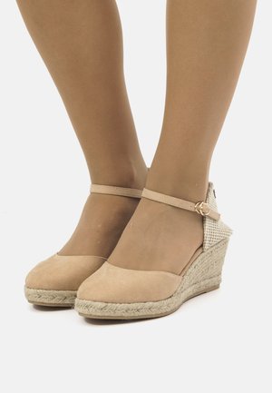 Zapatos de cuña de ante beige con una suela de yute trenzado, correa en el tobillo y acentos de tela a cuadros en el tacón. Textura suave y diseño de punta redondeada.