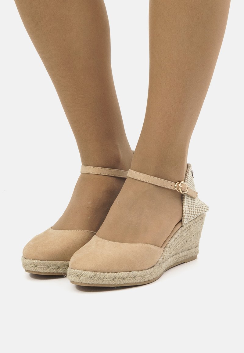 Zapatos de cuña de ante beige con una suela de yute trenzado, correa en el tobillo y acentos de tela a cuadros en el tacón. Textura suave y diseño de punta redondeada.
