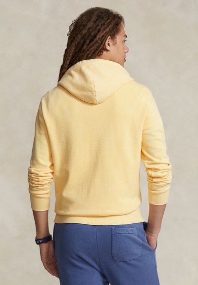 Κίτρινο φούτερ με κουκούλα, ριπ μανσέτες και τελείωμα, απαλής υφής, σε συνδυασμό με μπλε παντελόνι φόρμας με πίσω τσέπη. Καθημερινό, άνετο fit.