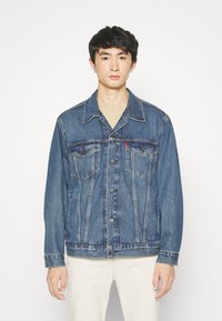 Chaqueta de mezclilla en azul oscuro con un cuello clásico, cierre de botones, dos bolsillos en el pecho y detalles de costura visibles. Textura suave.