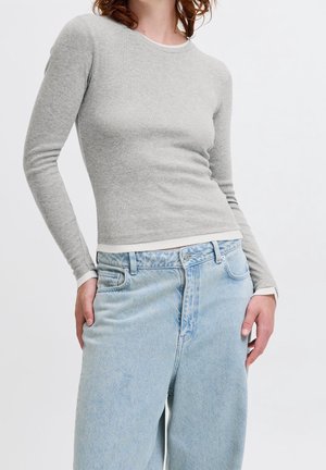 Grijze longsleeve van een zachte, aansluitende breistof met een ronde hals. Gecombineerd met lichtblauwe high-waisted jeans met een vervaagde textuur.