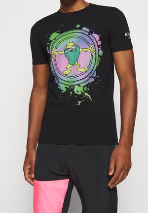 Black cotton t-shirt featuring a colorful cartoon graphic with splatter accents. The design includes a character with a green mask and arms outstretched.