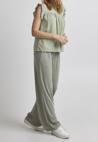 Top verde claro sin mangas con hombros con volantes y patrones texturizados, combinado con pantalones verdes holgados a juego y zapatillas blancas.