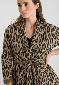 Cardigan de estampado de leopardo hecho de tela suave, con una cintura ceñida, cuello de chal y puños acanalados. Los tonos terrosos dominan el diseño.